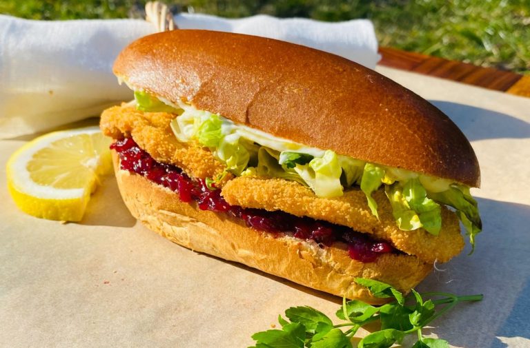 Brötchen mit paniertem Fisch, Salat, Preiselbeeren und einer Zitronenscheibe.
