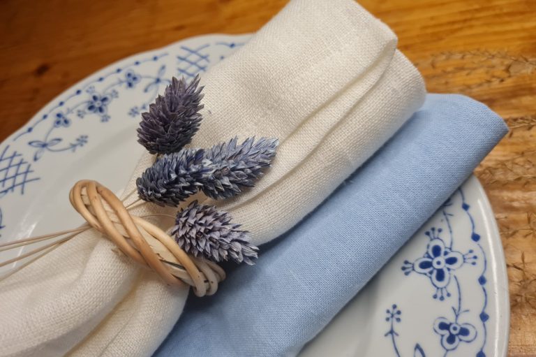 Gestapelte Servietten in blau und creme mit einem Juteband und kleinen Tannenzapfen.