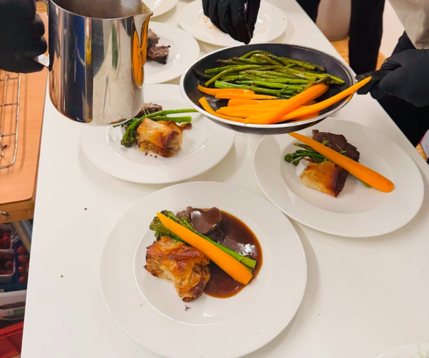 Ein Teller mit Fleisch, grünen Bohnen und Karotten wird angerichtet.